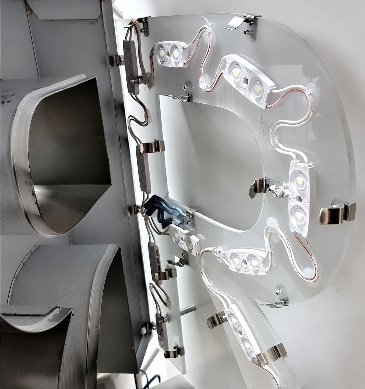Close-up photo of the back of a letter: a clear polycarbonate panel with LED modules and wiring, held to the aluminum extrusion return by stainless-steel clips